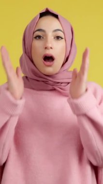 Surprised muslim woman in hijab looking at the camera in studio with yellow background