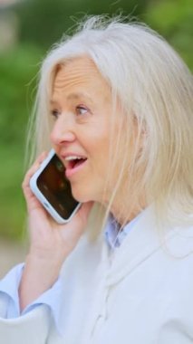 Yetişkin bir iş kadınının cep telefonuyla konuşurken gülümsediği dikey yavaş çekim videosu.