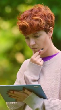 Parkta şüpheli bir yüze sahip dijital tablet kullanırken ayakta duran çift cinsiyetli olmayan kişi