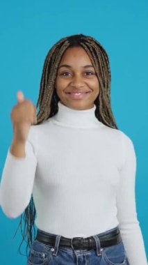 Afrikalı bir kadının mavi arkaplanlı videosu. Başparmağı havada, el kol hareketi yapıyor.