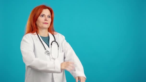 严肃而成熟的红头发女医生看着复印空间 蓝色背景 — 图库视频影像