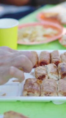 Güneşli bir günde parkta piknik masasından yemek alan isimsiz insanlar.