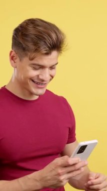 Stüdyoda sarı arka planı olan bir cep telefonu kullanırken gülümseyen, beyaz saçlı, mutlu, güçlü bir adam.