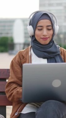 Kumandalı tesettürlü gülümseyen müslüman kadın bir karede oturan dizüstü bilgisayarla çalışıyor.