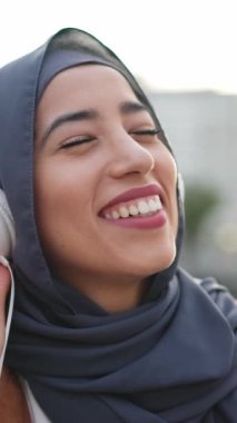 Müslüman kadın, şehir meydanında müzik dinlerken ve gülümserken yavaşça dans ediyor.