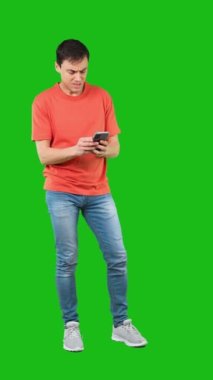 Gündelik kıyafetlerle dolaşan, kötü mesaj okuyan ve yeşil arka plana karşı akıllı telefondan tartışan bir erkek modelin tüm vücudu.