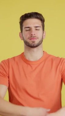 Kollarını kavuşturmuş beyaz bir adam stüdyoda sarı arka planda kameraya bakıyor.