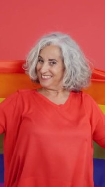 Studio video with red background of a mature woman wrapped with a lgbt rainbow flag