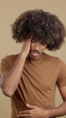 Studio image of a young man with hand on forehead expressing headache and stomachache