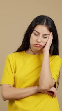 Bored hispanic woman standing and looking at the camera in studio with brown background