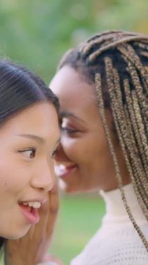 Slow motion video of an african woman tells friend a secret in her ear and makes a surprised face in a park