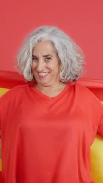 スペイン国旗を包みながらカメラを見ている笑顔熟女の赤い背景を持つスタジオビデオ — ストック動画