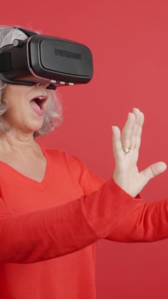 仮想現実のゴーグルを使用しながら 成熟した女性ジェスチャーの赤い背景を持つスタジオビデオ — ストック動画