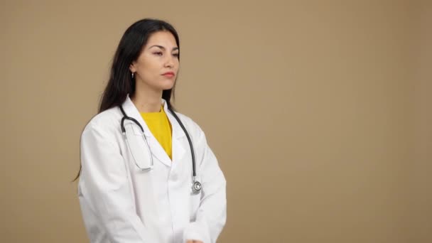 严肃的惊慌失措的女医生 双臂交叉 望着棕色背景的工作室 — 图库视频影像