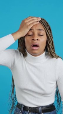 Video with blue background of a forgetful afro woman with her hand on her head gesturing a mistake
