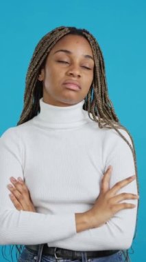 Video with blue background of an afro bored woman standing with her arms folded