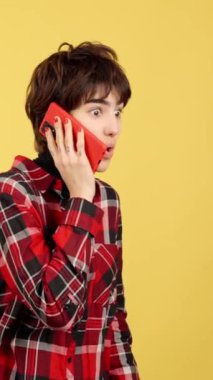 Stüdyoda sarı arka planlı cep telefonuyla konuşan çift cinsiyetli kişi şaşırdı.
