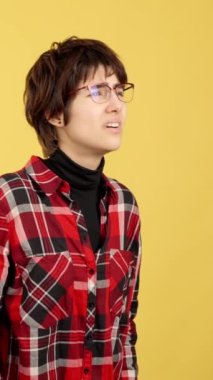 Androgynous sarı arka planlı stüdyoya bakmak için gözlüklerini çıkarıyor.