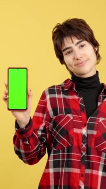 Androgynous sarı arkaplan ile yeşil mobil ekrana bakıyor