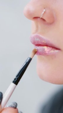 Bir kadının sahne arkasında fırçayla dudaklarına parlatıcı sürdüğü yavaş çekim videosu.