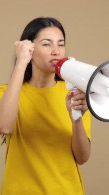 Upset caucasian woman yelling using a loudspeaker in studio with brown background