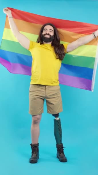 工作室视频 蓝色背景 一个笑容可亲的男人 假腿挥舞着彩虹Lgbt旗 — 图库视频影像