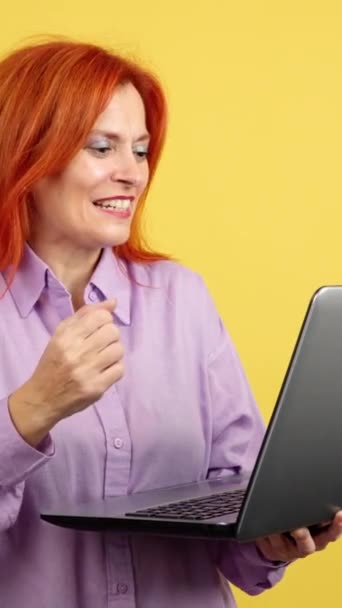 Зрелая Рыжая Женщина Празднует Глядя Ноутбук Студии Желтым Фоном — стоковое видео