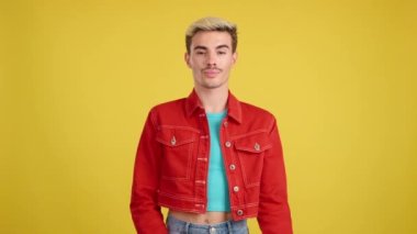 Stüdyoda kollarını kavuşturmuş, sarı arka planda neşeli eşcinsel adam poz veriyor.