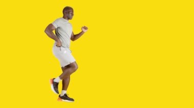 Stüdyoda sarı arka planda, diz egzersizi yapan Afrikalı güçlü bir adamın videosu var.