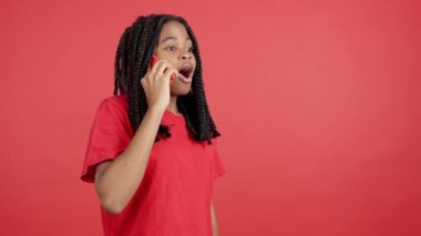 Stüdyoda kırmızı arka planda cep telefonuyla konuşan Afrikalı bir kadın.