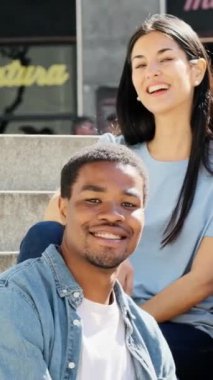 Bir kadın ve erkeğin şehir merdivenlerinde otururken kameraya gülümsediği yavaş çekim videosu.