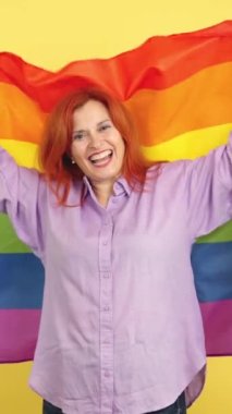Lgbt gökkuşağı bayrağıyla sarılı mutlu, kızıl saçlı, olgun bir kadın.