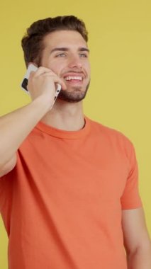 Stüdyoda sarı arka planda cep telefonuyla konuşan mutlu beyaz adam.