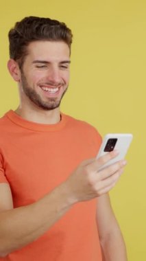Happy caucasian man smiling while using the mobile in studio with yellow background
