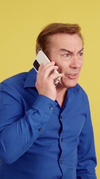 Angry Mature Man Talking Mobile Studio Yellow Background — Stockvideo