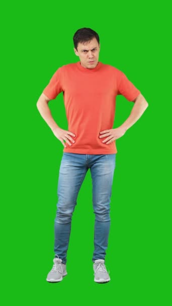 腰に手を置き怒りの表情を見せながら緑の背景にカメラを見ながら立つ屈辱的な男性モデルの全身 — ストック動画