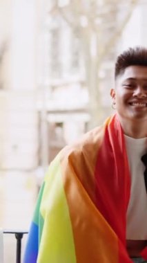 Elinde balkonda gülümseyen lgbt bayrağı olan İspanyol bir adamın yavaş çekim videosu.