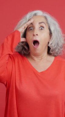 Studio video with red background of a mature woman looking at camera with a surprised look