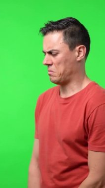 Kırmızı tişörtlü bir adam kameraya şüpheli ve şaşırmış bir şekilde bakıyor. Krom yeşil arkaplan, orta çekim.