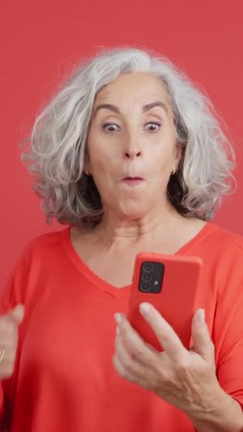 Studio Video Red Background Mature Woman Celebrating While Using Mobile — Vídeos de Stock