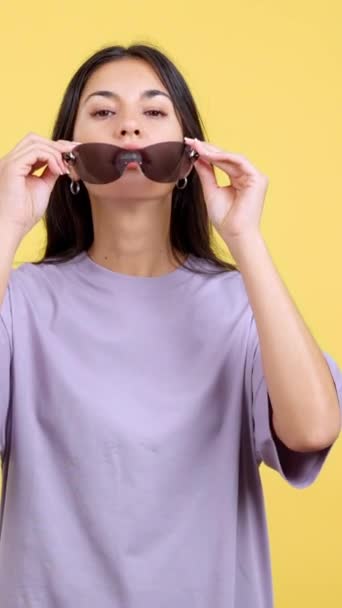 怒气冲冲的女人 戴着太阳镜看着黄色背景的摄影棚里的相机 — 图库视频影像