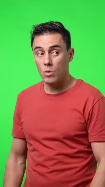 赤いTシャツの男が密かにカメラをオフに別の人に秘密をささやく クロマグリーンの背景 ミディアムショット — ストック動画