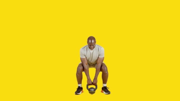 Film Studio Żółtym Tłem Afrykańskiego Sportowca Robi Przysiady Kettlebell — Wideo stockowe