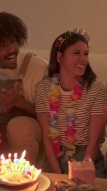 Arkadaşları evde şarkı söyleyip kucaklaşırken doğum günü pastasının mumlarını üfleyen bir kadının yavaş çekim videosu.