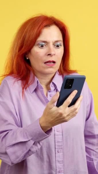 Удивлённая Рыжая Зрелая Женщина Смотрящая Экран Мобильного Телефона Студии Жёлтым — стоковое видео