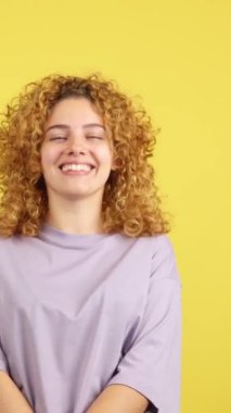 Studio video with yellow background of a beuty woman with curly hair and casual clothes laughing