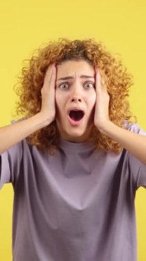 Studio video with yellow background of a beauty woman with curly hair gesturing with the hands on the face expressing dismay