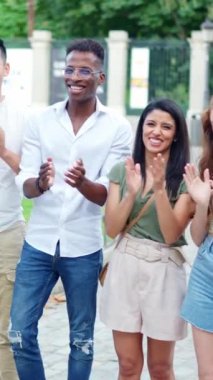 Group of multiethnic friends applauding while looking at the camera outdoors