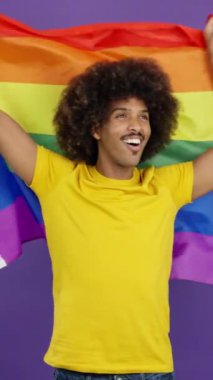 Happy african man raising a lgbt rainbow flag while looking at the camera in studio