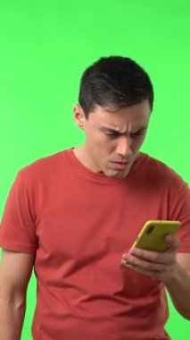 Koyu renk saçlı, yeşil arka planda duran ve kötü haberlerle mesaj alan hoş olmayan genç adam.